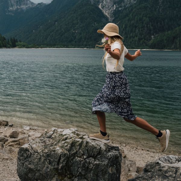 Woman by the side of a lake in a summery outdoor outfit and balancing on small rocks