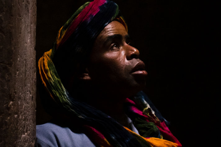 A man wearing a turban leaning against a wall in the dark